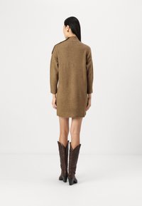 Brun strikket kjole med høy krage og trekvart erm, sammen med brune cowboystøvler med spiss tå og teksturerte detaljer.