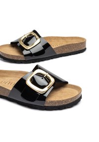 Sandales à glissière en patent noir avec une large sangle ornée d'une boucle dorée. Semelle en liège et semelle extérieure en caoutchouc noir texturé.