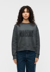 Γκρι φούτερ με κομψό κοντό σχέδιο, με μεγάλο μαύρο λογότυπο μπροστά. Μακρυά μανίκια και απαλό, υφασμένο ύφασμα.