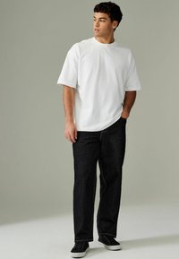 Hvid kortærmet t-shirt kombineret med mørke denim jeans og sorte sneakers. Jeansene har lige pasform og synlige stikninger.
