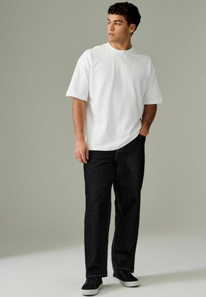 Hvid kortærmet t-shirt kombineret med mørke denim jeans og sorte sneakers. Jeansene har lige pasform og synlige stikninger.