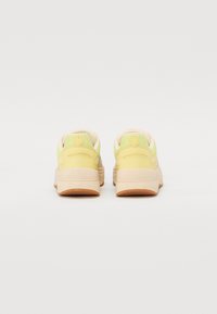 Sneaker con una toma superiore in rete gialla con accenti pastello chiari, una suola testurizzata e un design arrotondato con un logo sul retro.
