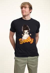 Černé tričko s plyšovým designem postavičky Sooty, s hnědými a bílými akcenty a velkým červeným a žlutým textem "Sooty" pod ním.