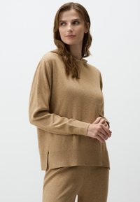 Maglietta a maniche lunghe color marrone chiaro con una vestibilità rilassata, polsini a coste e spacchi laterali. Tessuto morbido e design semplice, abbinata a pantaloni coordinati.
