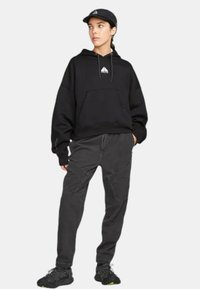 Svart huvtröja med ficka fram och logotyp, i kombination med grå cargobyxor med texturerade paneler och svarta sportskor.