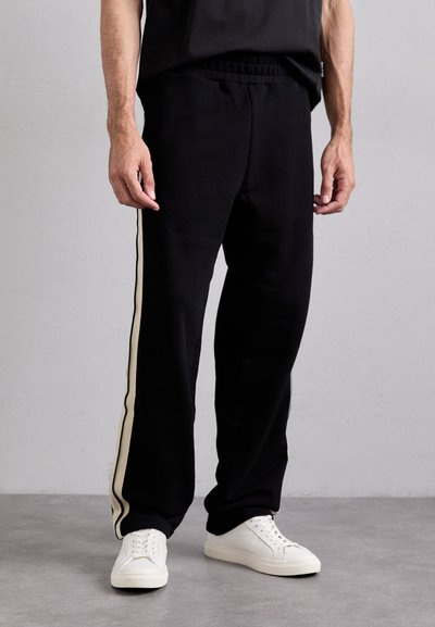 Zwarte sportbroek met een relaxte pasvorm, voorzien van twee verticale crème strepen langs de buitenzomen. Elastische tailleband en eenvoudig ontwerp.