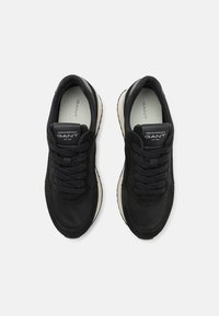 Baskets de sport noires avec une tige en daim et en tissu, bout rond et semelle épaisse couleur crème. Présente des lacets noirs et un logo sur la languette.