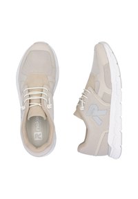 Baskets de sport beiges avec une tige en mesh, des accents en daim, un logo réfléchissant et une semelle en caoutchouc blanc avec un motif de texture.