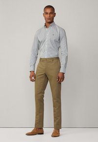 Camicia a righe bianche e blu chiaro con bottoni, pantaloni beige e mocassini in suede marrone. Design semplice con una silhouette aderente.