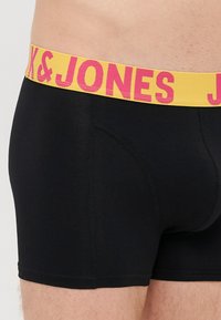 Černé boxerky s žlutým páskem a růžovým brandingem "K&JONES". Vyrobeno z pružného materiálu s hladkou texturou.