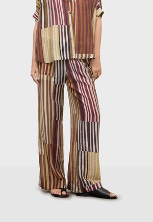 Bukser med løs pasform med flerfarvede lodrette og vandrette striber i sennepsgul, bordeaux, beige og sort, kombineret med en matchende skjorte med knapper.