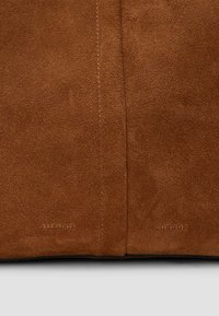 Materiale scamosciato marrone con una texture liscia. Include il marchio in rilievo "ALLSAINTS" e "LONDON" vicino al bordo inferiore.