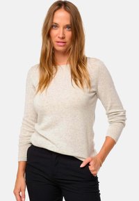 Pull long à manches longues beige clair en tricot doux et texturé ; col rond et coupe décontractée, accompagné d'un pantalon noir.