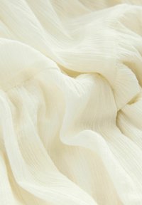 Tessuto bianco sgualcito con una texture morbida e trasparente. Il materiale ha un aspetto leggero e fluttuante con sottili variazioni di tonalità.