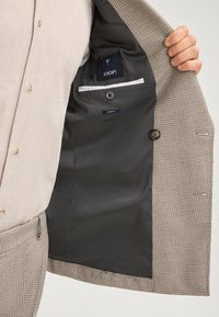 Beżowa marynarka w kratę z ciemnym podszewką. Posiada dwa guziki, wewnętrzną kieszeń oraz metkę z napisem "Slim Fit" i "JOOP!".