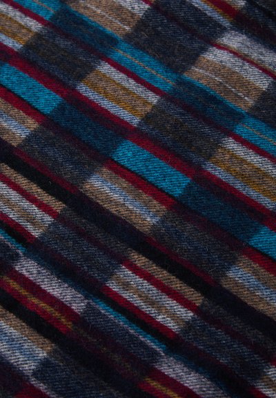 Vilnonė tekstilė su daugiakampiu raštu, kuriame derinami tamsiai mėlyna, raudona, turkio, ruda ir pilka juostelės. Minkšta tekstūra su audimo išvaizda.