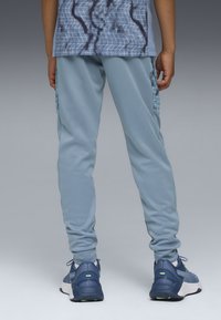 Helle blaue Sporthose mit glatter Textur, ausgestattet mit Seitentaschen mit strukturiertem Muster. Kombiniert mit blauen Sneakers.