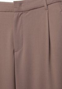 Gros plan sur un pantalon taupe sur mesure montrant la ceinture, la couture latérale, l'ouverture de la poche et les détails du pli avant.