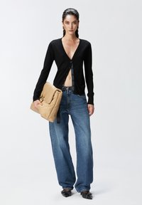 Cardigan nero a maglia con scollatura a V profonda, chiusura con bottoni, abbinato a jeans denim blu a vestibilità rilassata. Borsa beige trapuntata con tracolla nera.