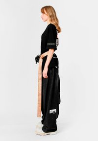 Camiseta negra de gran tamaño, con gráfico en la espalda. Pantalones anchos negros con bolsillos laterales. Cinturón beige con letras. Zapatos blancos gruesos.