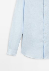 Camicia button-up azzurro chiaro con un delicato motivo a righe, maniche lunghe e orlo curvo con una texture morbida.