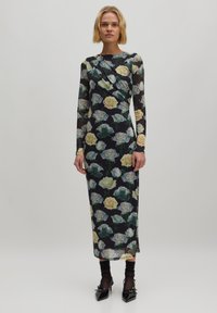 Langärmliges Blumenkleid aus transparenter Stoff, mit einem dunklen Grundton und gelben sowie grünen Rosen. Figurbetonte Silhouette mit Raffung im Schulterbereich.