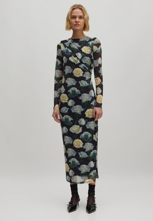 Langärmliges Blumenkleid aus transparenter Stoff, mit einem dunklen Grundton und gelben sowie grünen Rosen. Figurbetonte Silhouette mit Raffung im Schulterbereich.