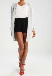 Světle šedý pletený cardigan, bílý top, černé kraťasy s krajkovým lemováním a červené lakované sandály na podpatku s pásky. Jednoduchý, neformální outfit.