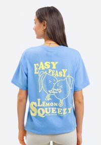 Svetlomodré bavlnené tričko so grafickým dizajnom dvoch citrónov s hravými výrazmi a textom "Easy Peasy Lemon Squeezy" v žltej farbe.