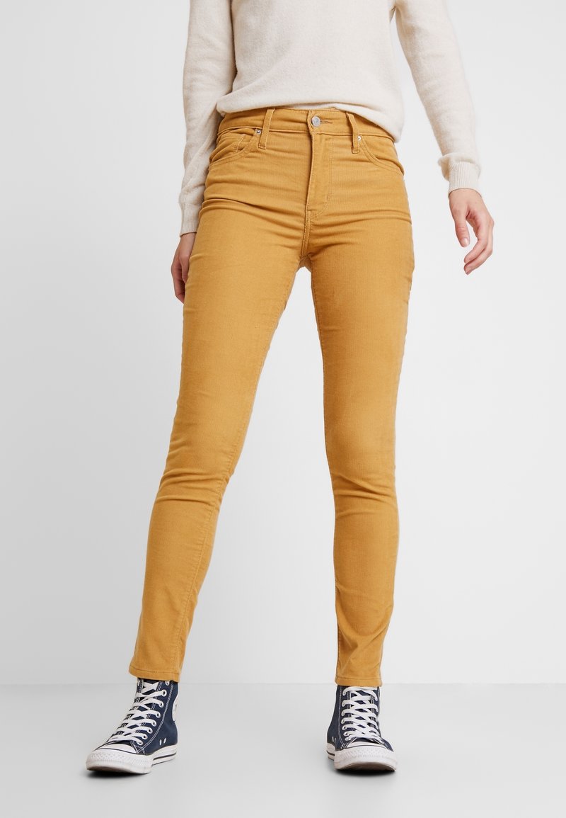 Jeans ajustados de color mostaza, hechos de una mezcla de algodón con una textura suave, que cuentan con un clásico diseño de cinco bolsillos y cierre de cremallera.