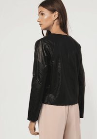 Chaqueta de cuero negra con mangas largas, cuello redondeado y textura lisa, combinada con pantalones rosa claro. Silueta ajustada en general.