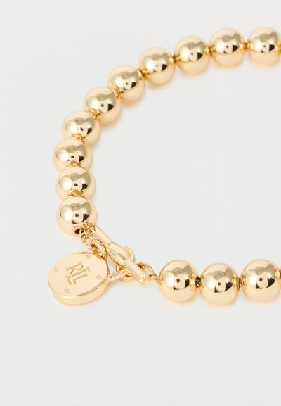 Bracelet en perles dorées avec des perles rondes et un fermoir à bascule comportant un charme circulaire gravé des initiales « RL ».