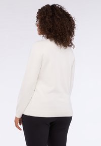 Maglione color crema con una texture soffice, maniche lunghe e polsini e orlo a coste. Presenta una vestibilità rilassata e elementi di design minimal.