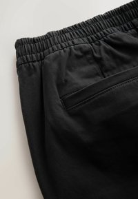 Black pants featuring a wide, elastic waistband, smooth texture, and a single rear pocket with subtle stitching detail.
