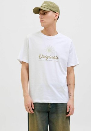 Hvid bomulds t-shirt med guld "Originals" tekst og stjernes grafik. Sammen med en olivengrøn kasket og løstsiddende jeans. Glat tekstur.