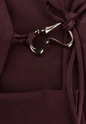 Donkerpaars stof gebonden met twee geknoopte riemen die zijn verbonden door een glanzende, gebogen metalen gesp.