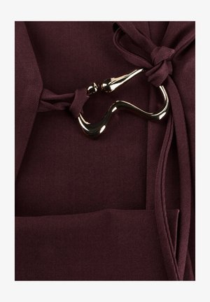 Donkerpaars stof gebonden met twee geknoopte riemen die zijn verbonden door een glanzende, gebogen metalen gesp.