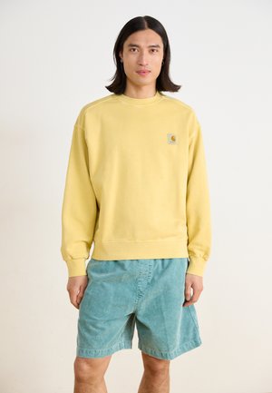 Hellgelbes Sweatshirt mit gerippten Bündchen und Saum, versehen mit einem kleinen Logo auf der Brust, kombiniert mit türkisfarbenen Shorts aus weichem Material.