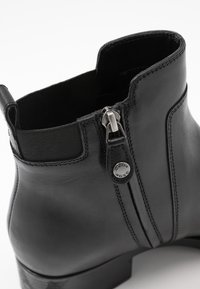 Botín de cuero negro hasta el tobillo con cremallera lateral, panel elástico, acabado suave y punta redonda. Detalle notable del logo en el tirador de la cremallera.