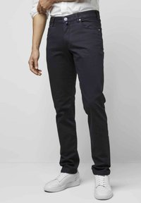 Jeans en denim bleu foncé avec une coupe slim, un design à cinq poches et des détails de bouton contrastants, associés à des baskets blanches.