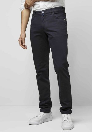 Dunkelblaue Denim-Jeans mit schlankem Schnitt, Fünf-Taschen-Design und kontrastierenden Knopfdetails, kombiniert mit weißen Sneakers.