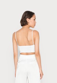 Top branco cropped com alças finas e costas franzidas, apresentando um design limpo e uma textura suave. Combinado com calças brancas.