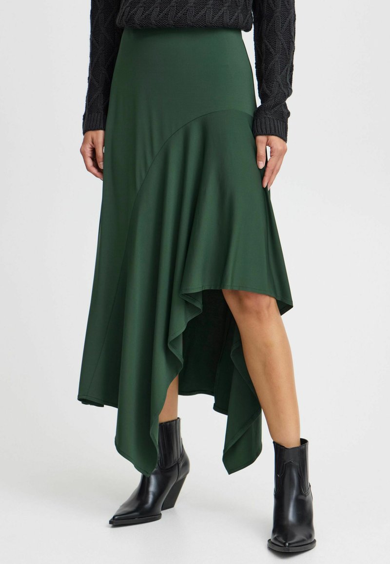 Asymmetrisk grön kjol i draperad jerseytyg, med en hög-låg fåll och parat med svarta ankelstövlar. Texturen verkar slät.