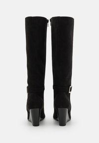 Bottes noires en suede jusqu'au genou avec fermeture éclair, dotées d'une sangle et d'une boucle, et d'un design à talon épais.