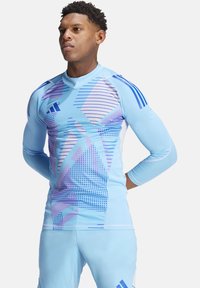 Hellblaues Sportshirt mit langen Ärmeln, das ein geometrisches Design in Lila und Blau aufweist und aus einem dehnbaren, strukturierten Material gefertigt ist.