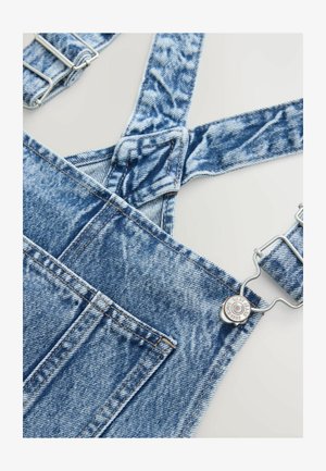 Denim ülemdressid reguleeritavate rihmadega, helesinise tooniga ja hõbedaste detailidega. Omab taskut ja kulumisjälgi kangal.