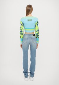 Kratka sv sweaters, pletena v svetlo modri barvi, z dolgimi zelenimi rokavi, ki imajo modre vzorce. V kombinaciji s svetlo modrimi naravnost krojenimi kavbojkami.