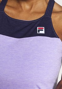 Lila sportstopp med en mörklila övre del, ljuslila nedre del och en Fila-logotyp på vänster sida. Slät textur, justerbara remmar.