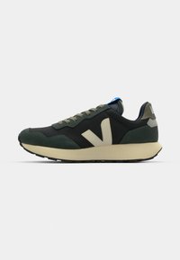 Black and green sneaker with a textured upper, round toe, beige accents, and a cushioned beige sole. Features lace-up design and blue tag.