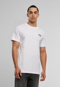 Witte katoenen T-shirt met korte mouwen en een ronde hals, voorzien van een klein zwart tekstafbeelding op de linkerkant van de borst.